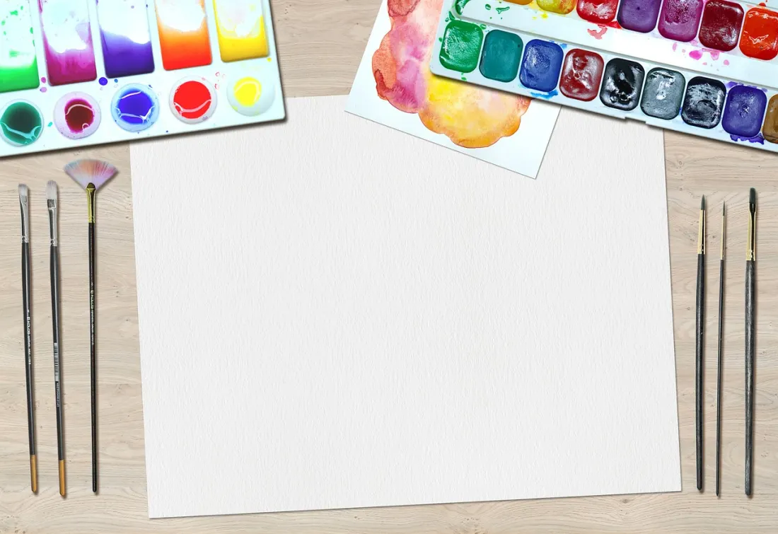 Watercolour pans, brushes and blank paper on a wooden table