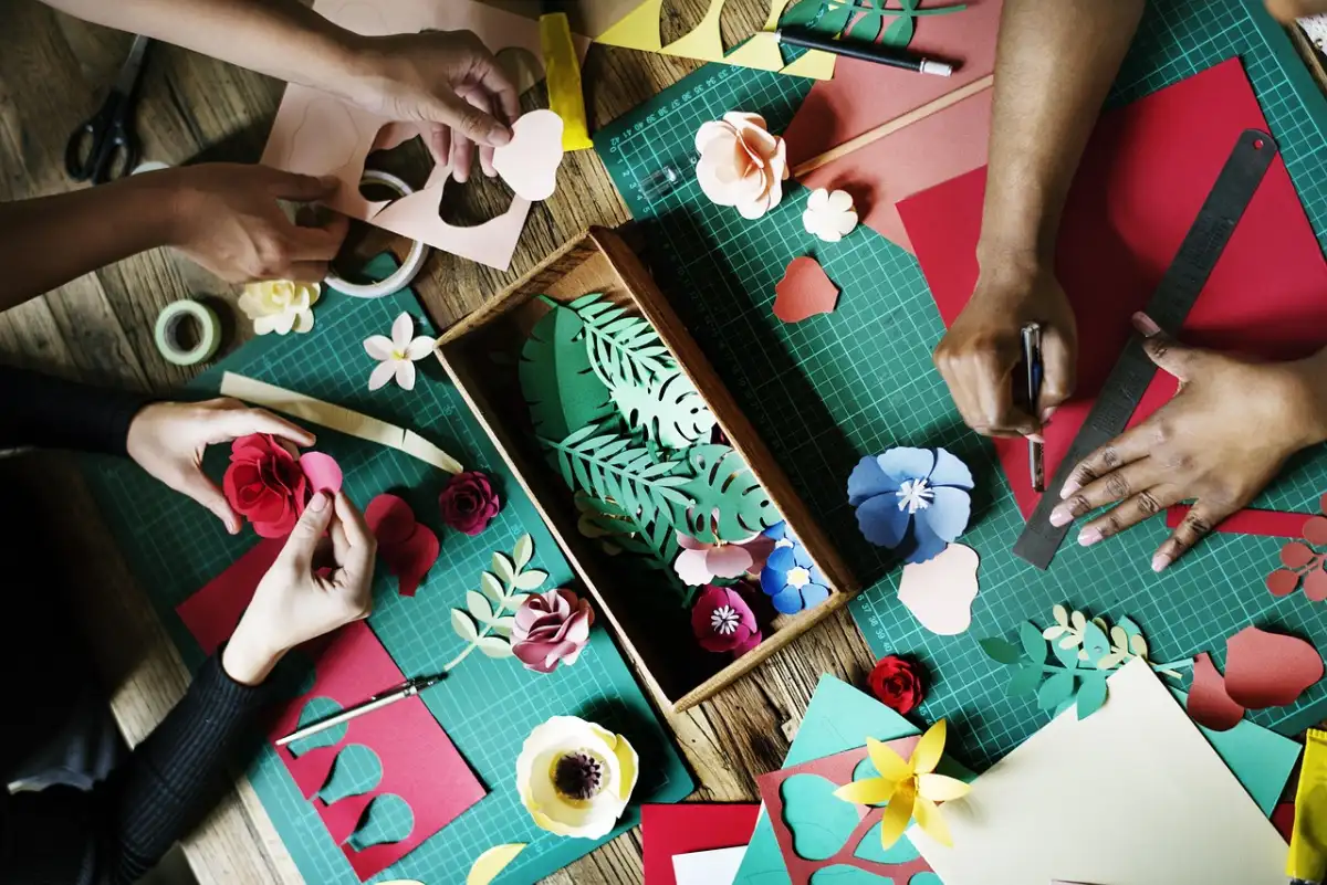 Overhead view of many small hands cutting paper leaves at a craft table