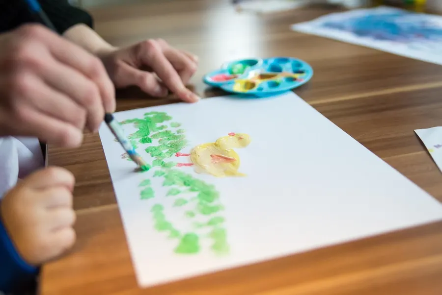 Children painting green shapes on paper at a wooden table