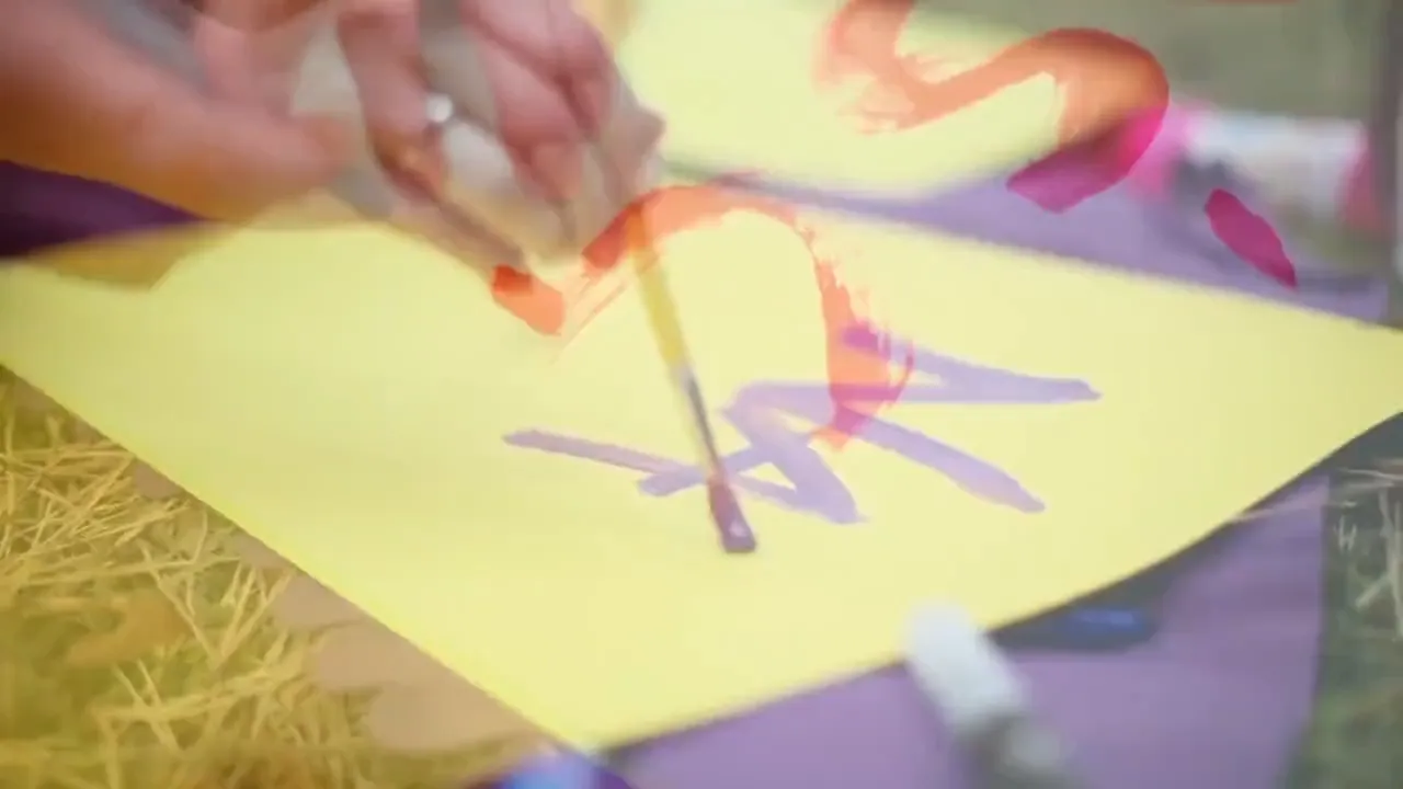 A child's hand painting letters on bright yellow paper