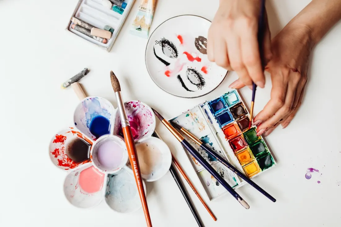 Hands mixing paint on a flower-shaped palette among brushes